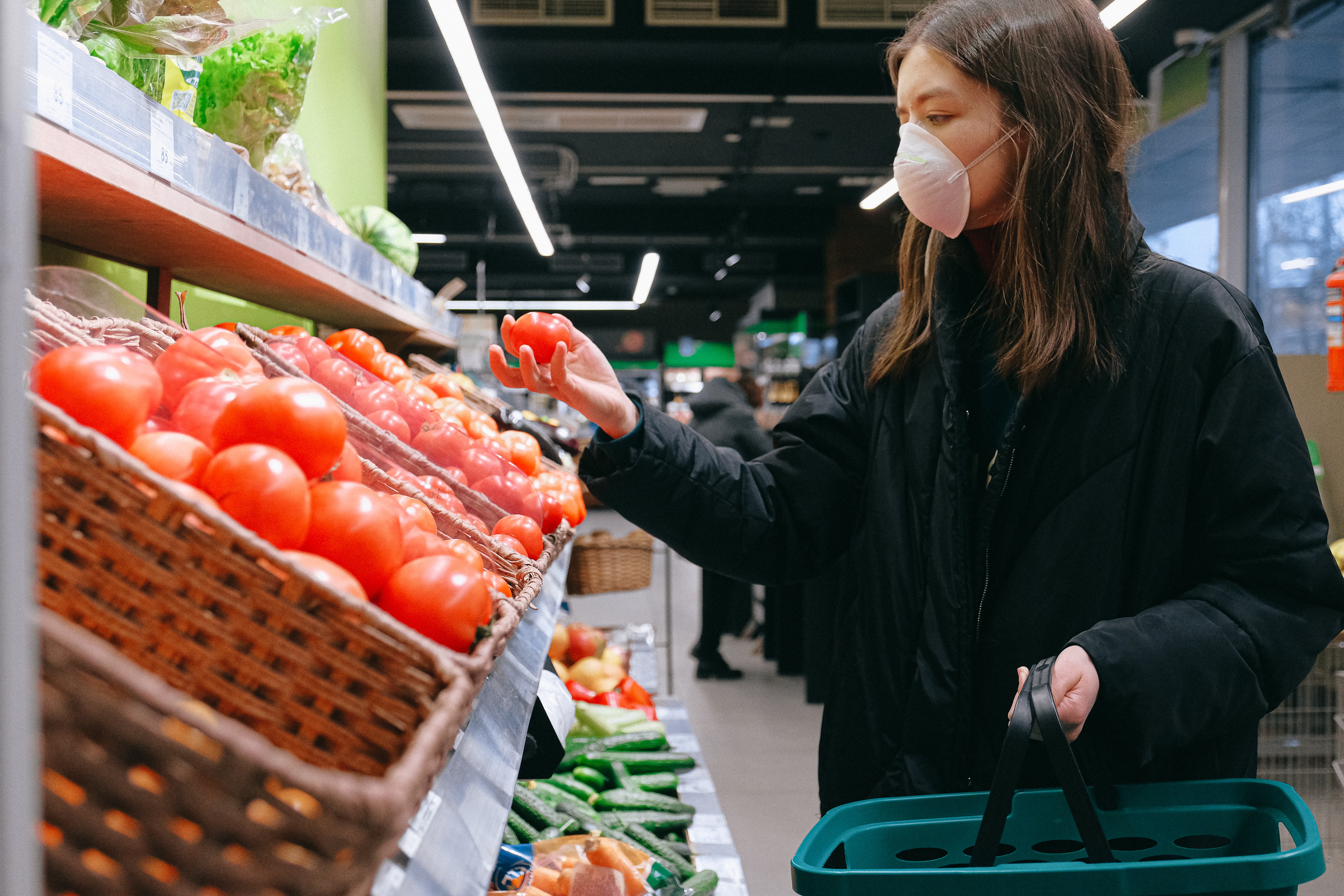 Woman wearing mask in supermarket shopping for tomatoes